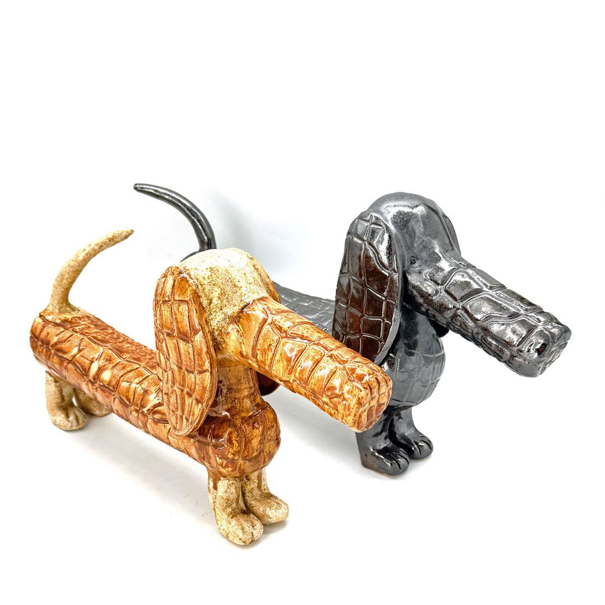 Twee decoratieve sculpturen in de vorm van een teckel, een beige en een grijze.