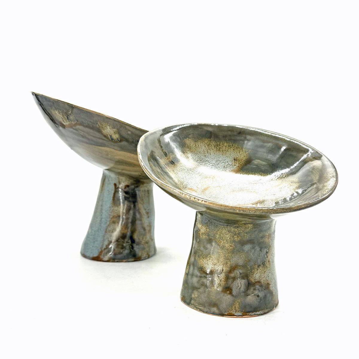 Twee kleine metalen schaaltjes op een voetstuk, een schuin en een ondiep schaaltje, op een witte achtergrond.