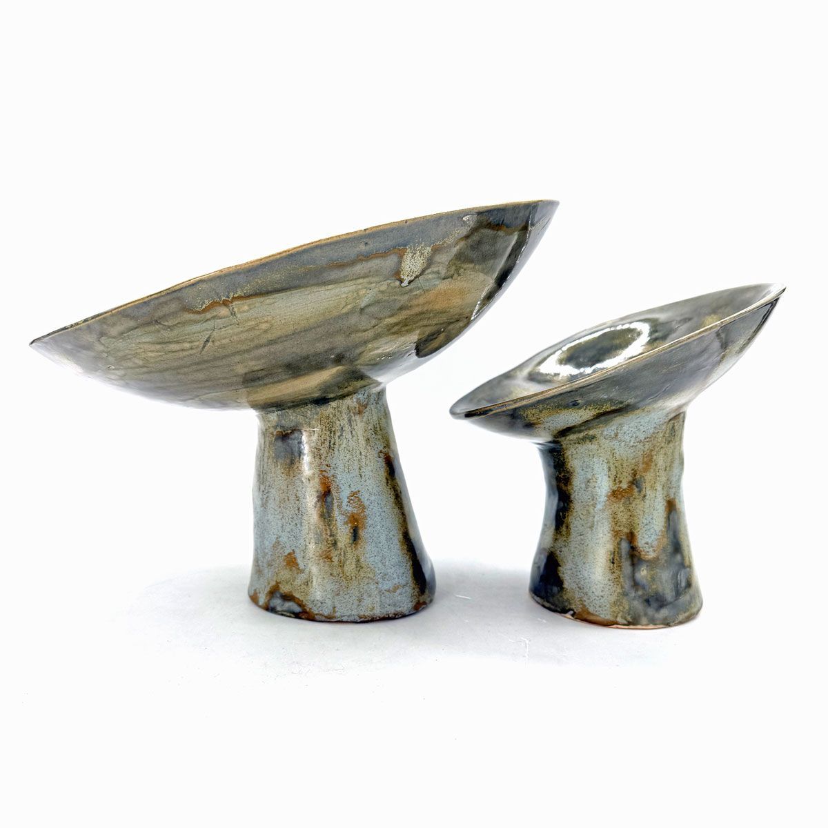 Twee kleine, abstracte metalen sculpturen met schuine bovenzijden en smalle sokkels op een witte achtergrond.