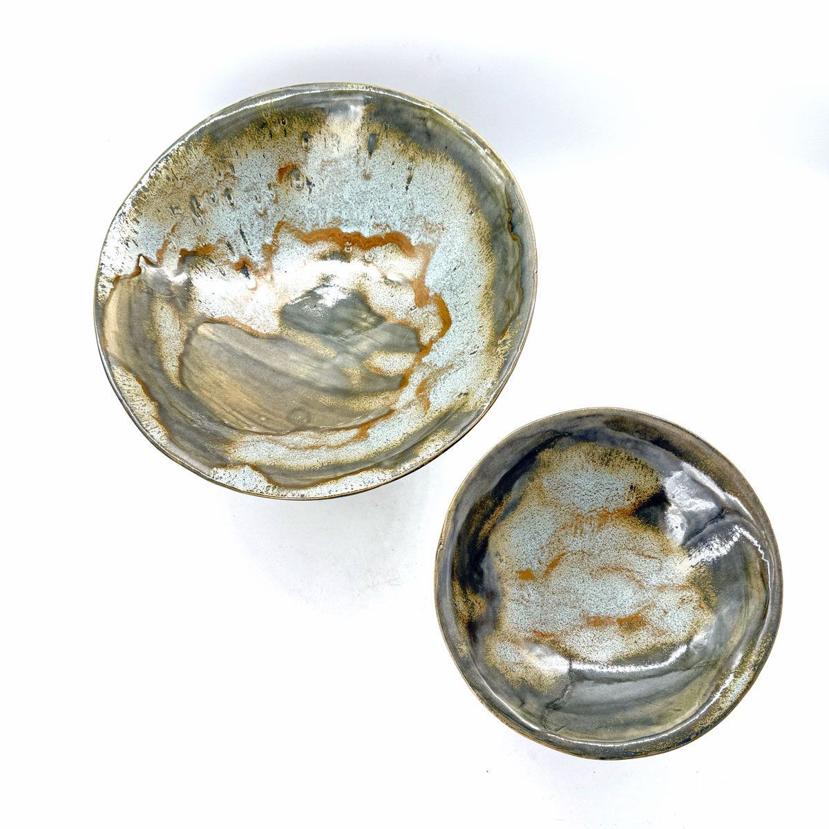 Twee kleine ronde keramische schaaltjes met een grijs, goud en wit gemarmerd glazuur op een witte achtergrond.