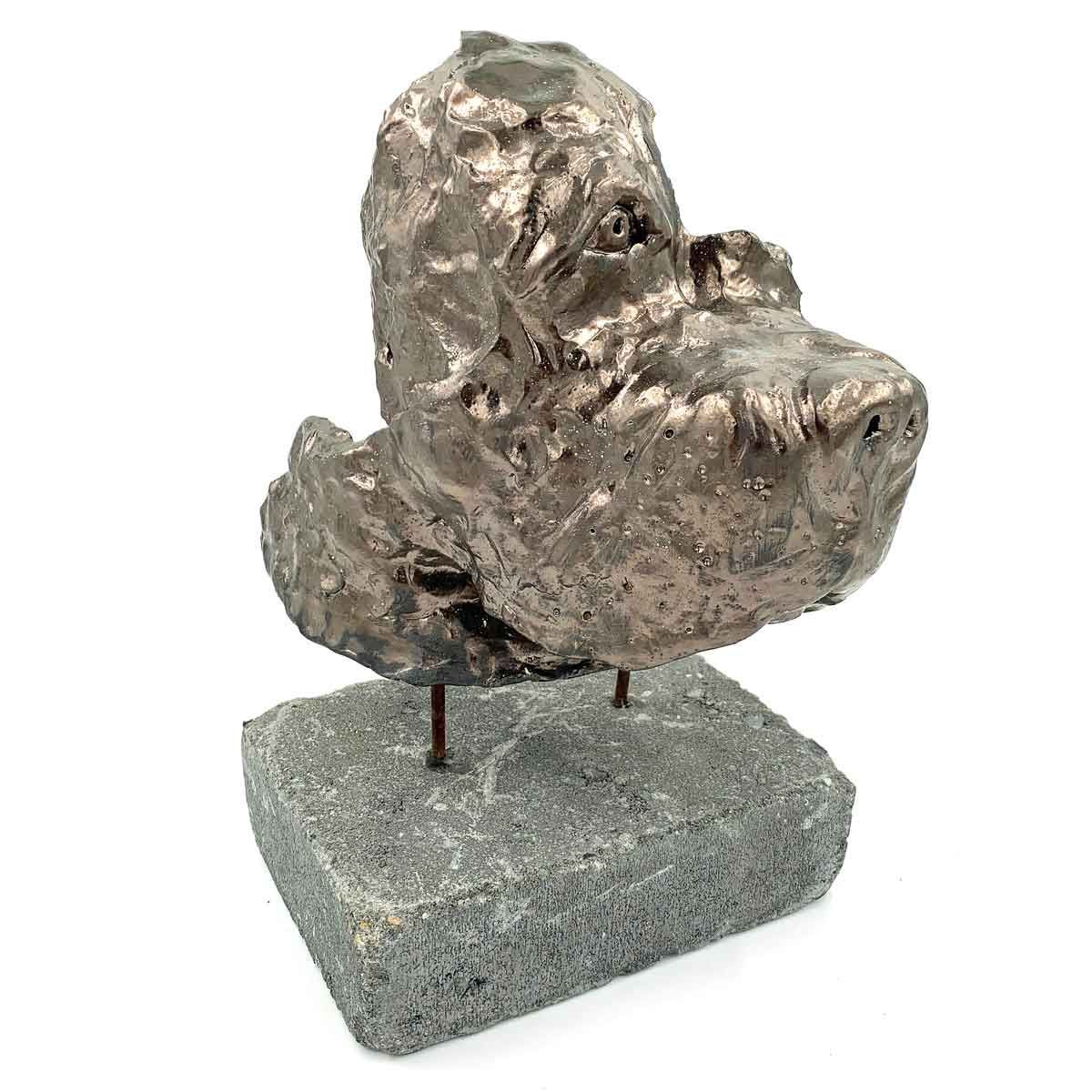 Abstracte metalen sculptuur op een grijze stenen sokkel met twee zichtbare steunpinnen.