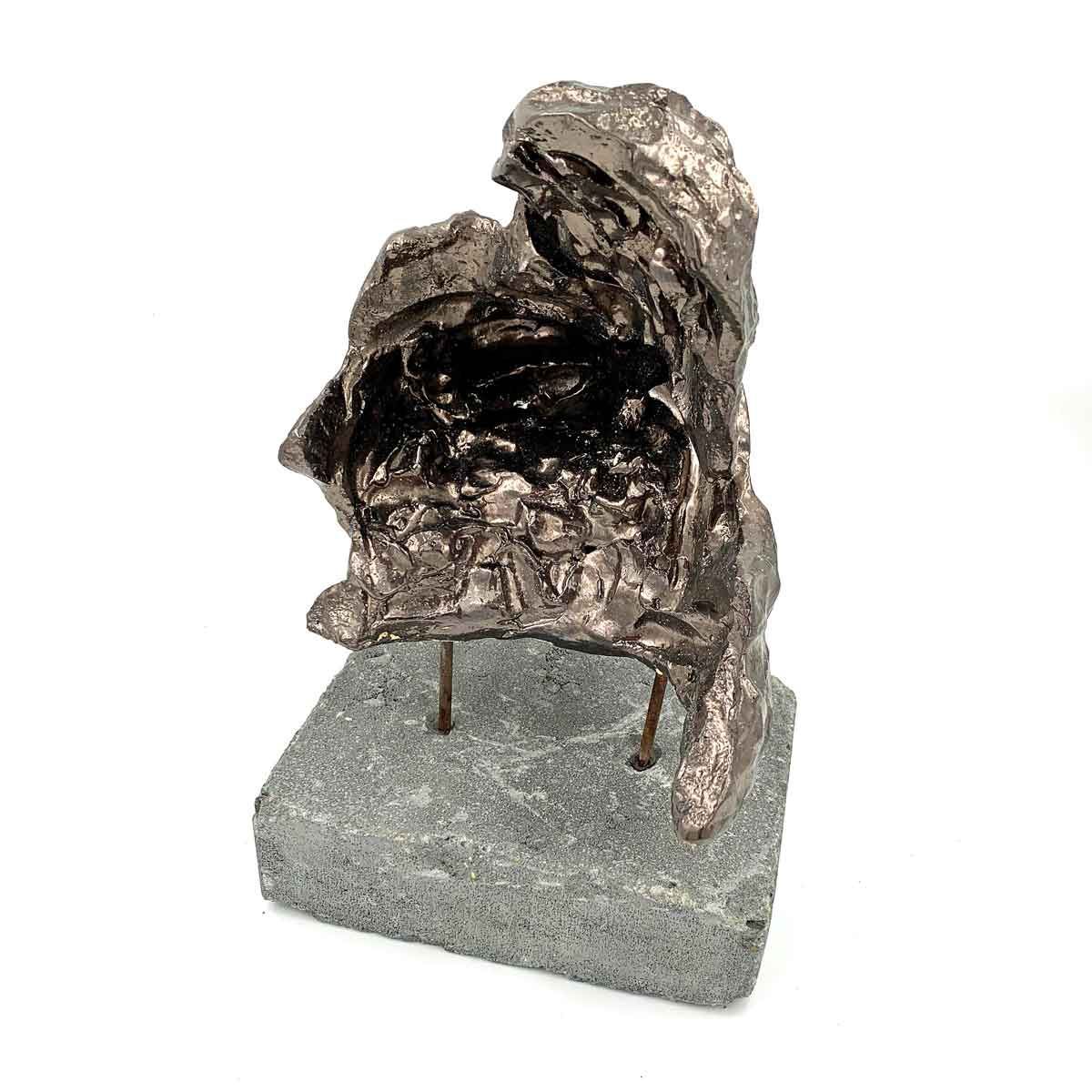 Abstracte, donkere metalen sculptuur op een grijze sokkel tegen een witte achtergrond.