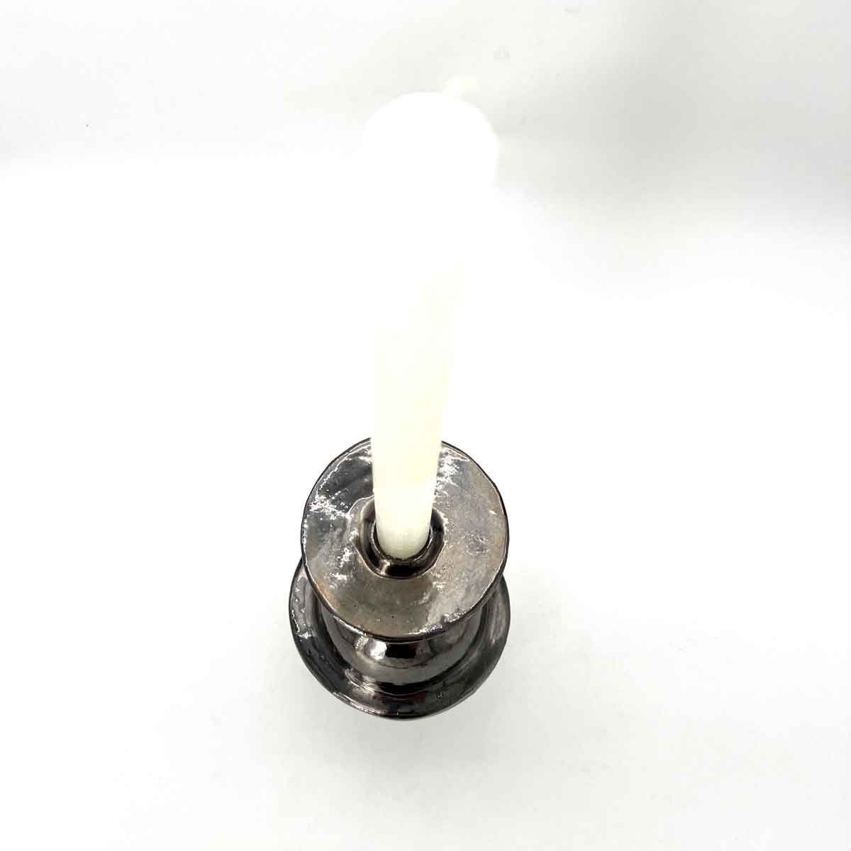 Close-up van een witte kaars in een donkere metalen houder op een witte achtergrond.