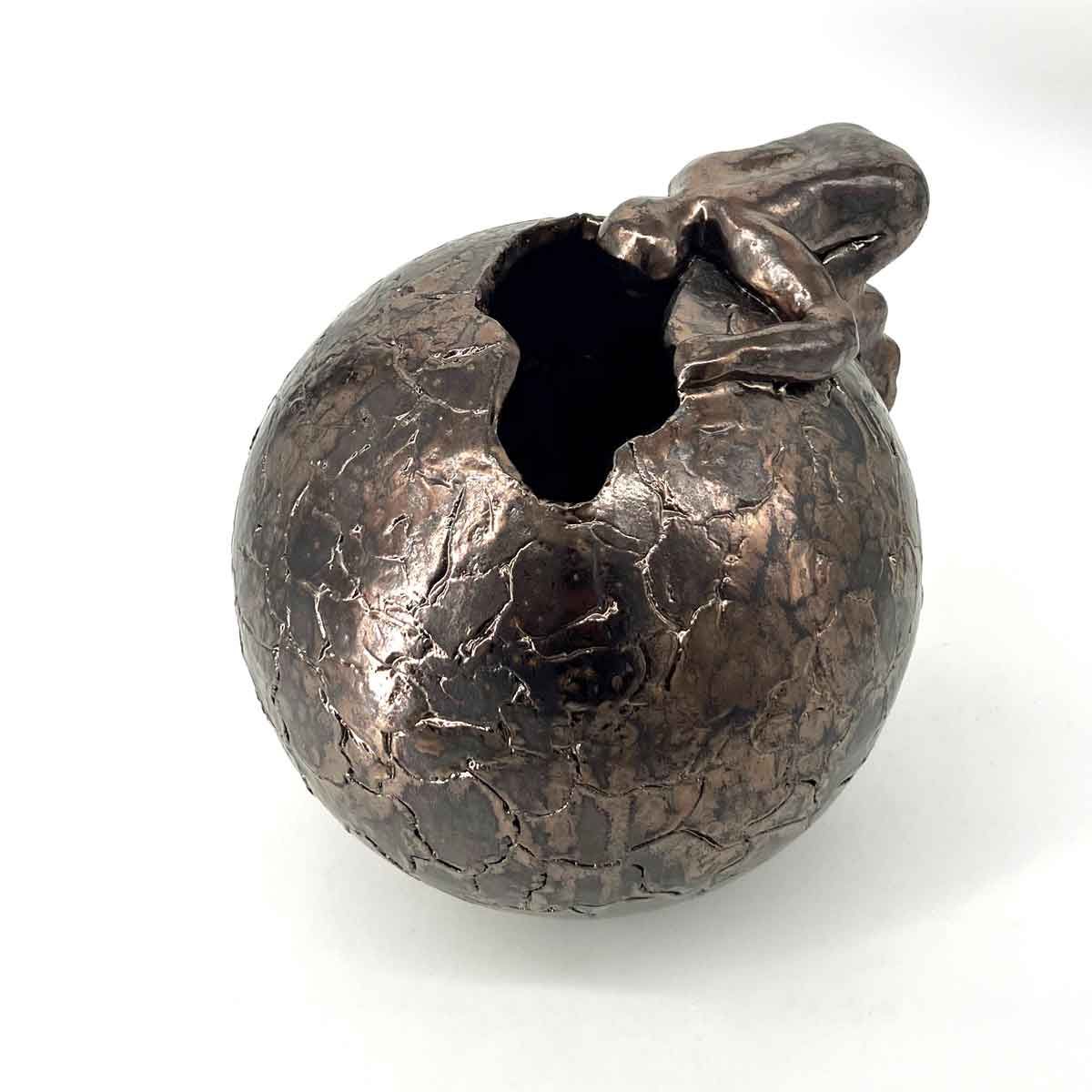 Een gebarsten donkere metalen bol met een klein gebeeldhouwd vogeltje erop, geïsoleerd op een witte achtergrond.