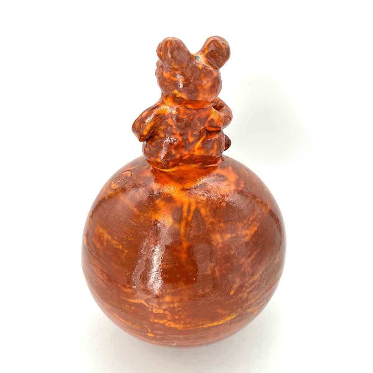 Amberkleurige fles met een ronde voet en een kleine, diervormige stop bovenop.