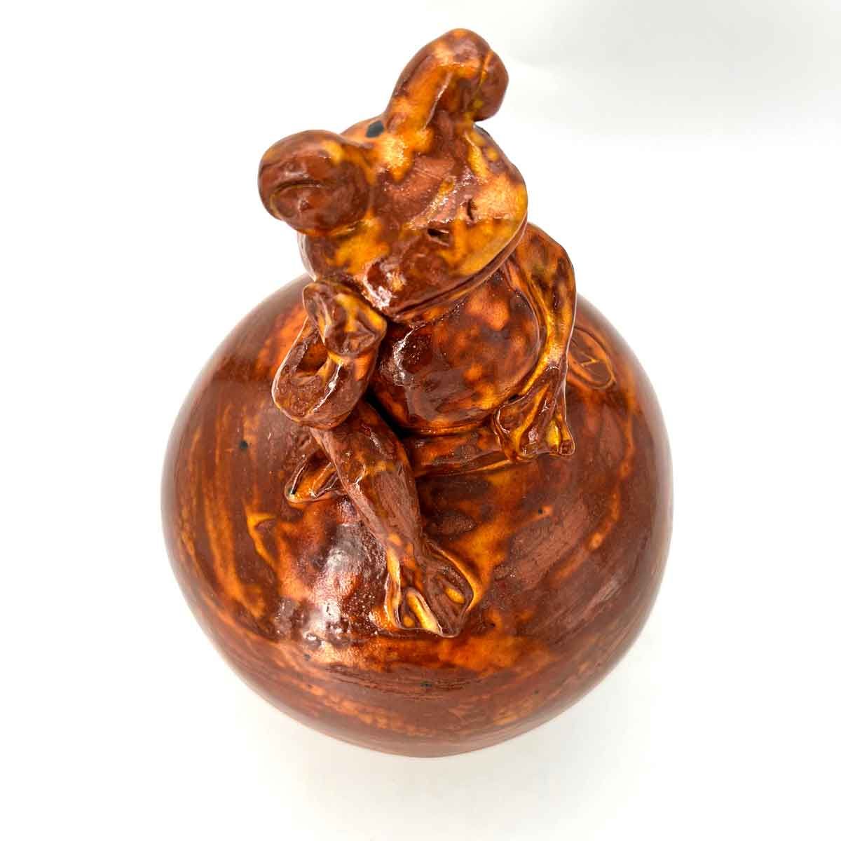 Amberkleurig beeldje van een persoon die een ronde bol beklimt op een witte achtergrond.