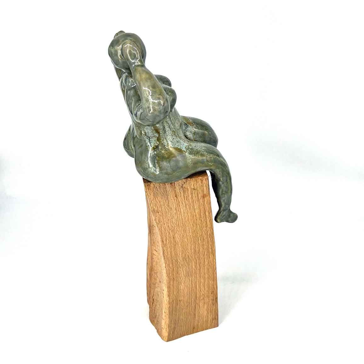 Klein groengrijs beeldje zittend op een houten blokje tegen een witte achtergrond.
