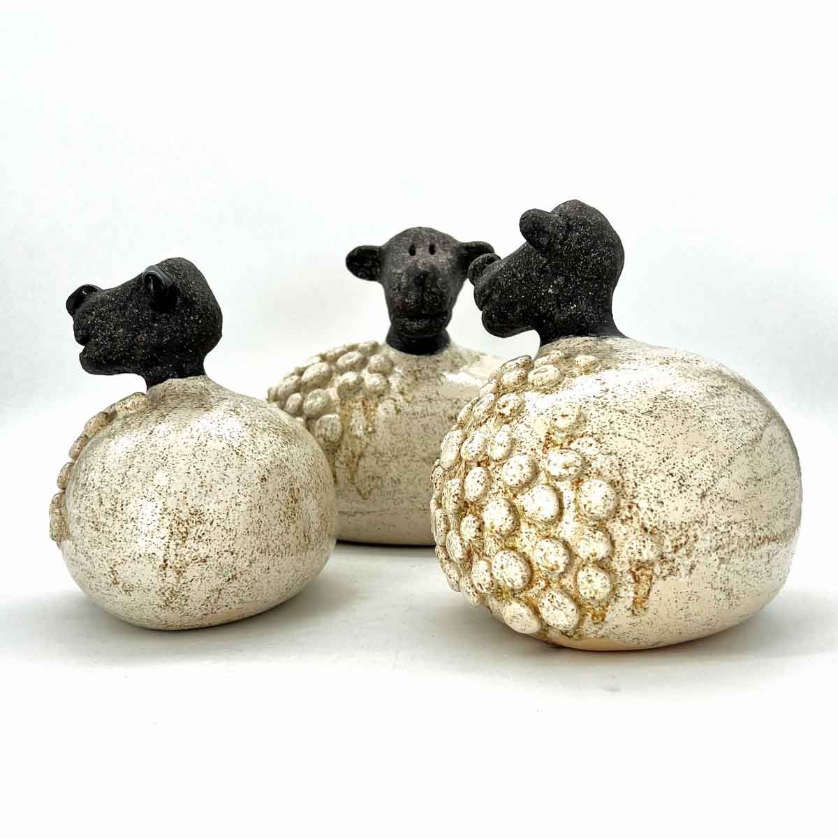 Drie zwartkoppige schaapjesfiguurtjes op gespikkelde witte bollen tegen een witte achtergrond.