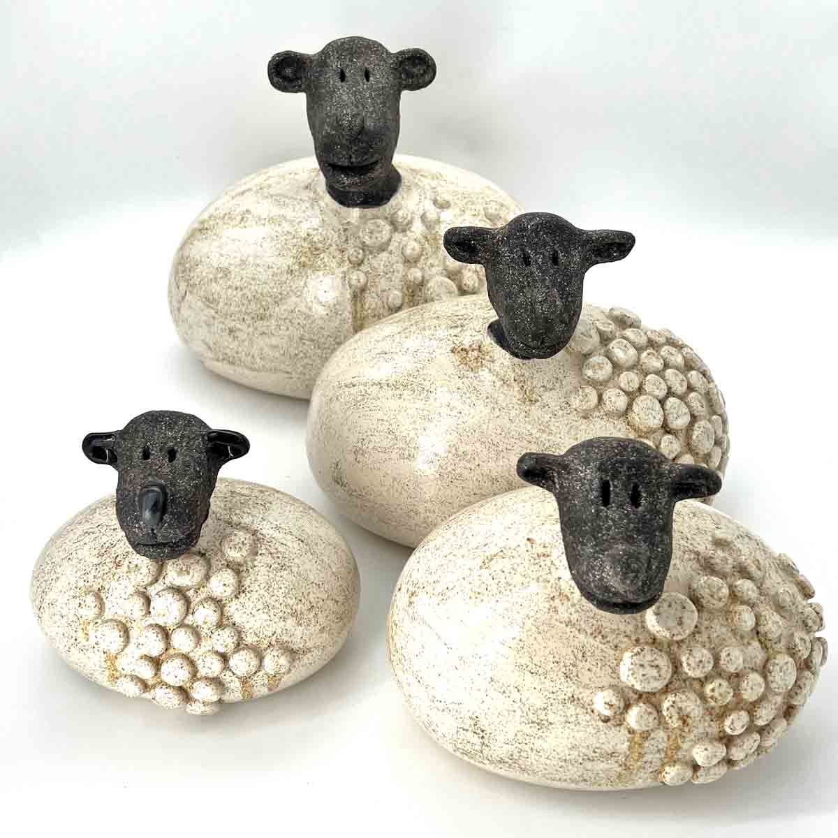 Vier decoratieve schaapjes met zwarte koppen en witte, gestructureerde lichamen op een witte achtergrond.