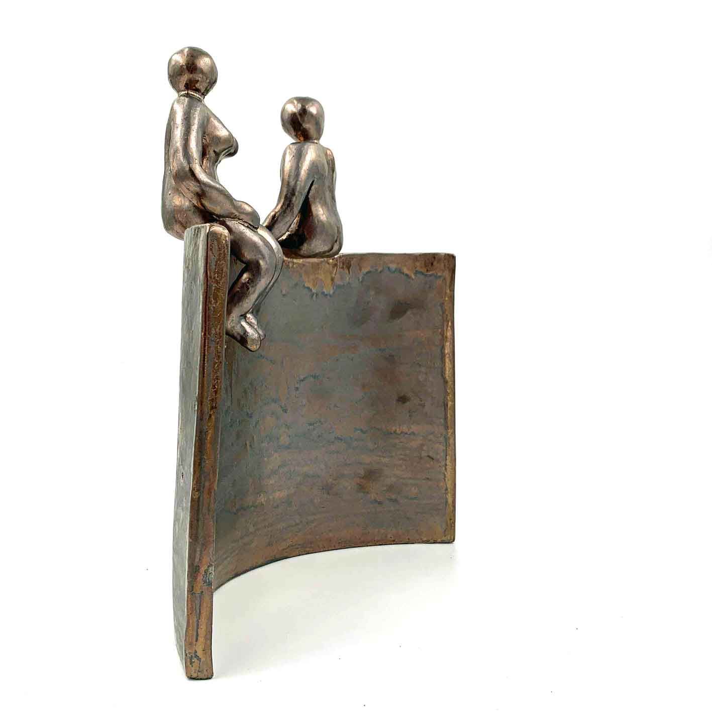 Twee kleine bronzen beeldjes zitten bovenop een gebogen metalen sculptuur op een witte achtergrond.