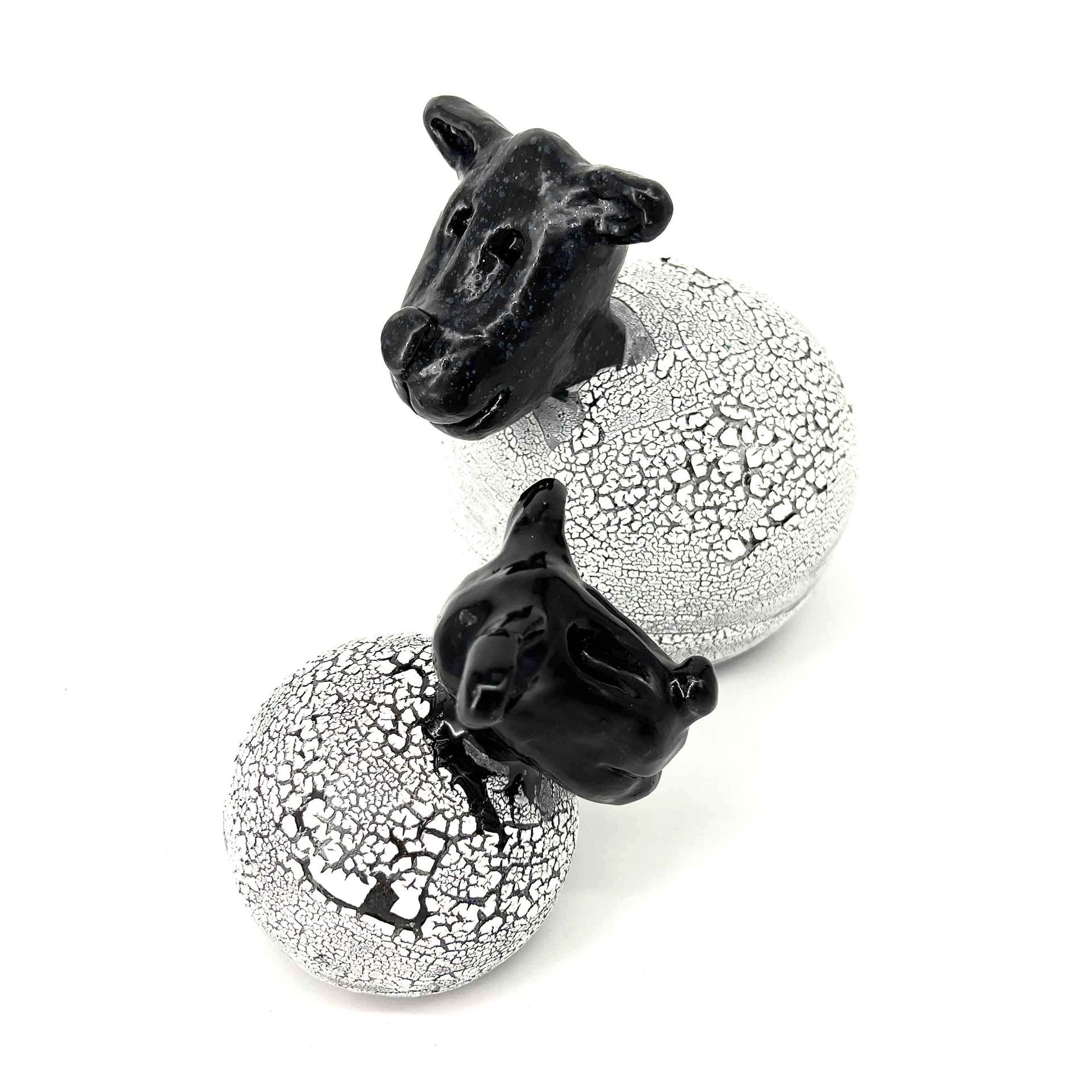 Twee kleine zwarte hondjes op gebarsten witte bollen, de ene achter de andere staand.