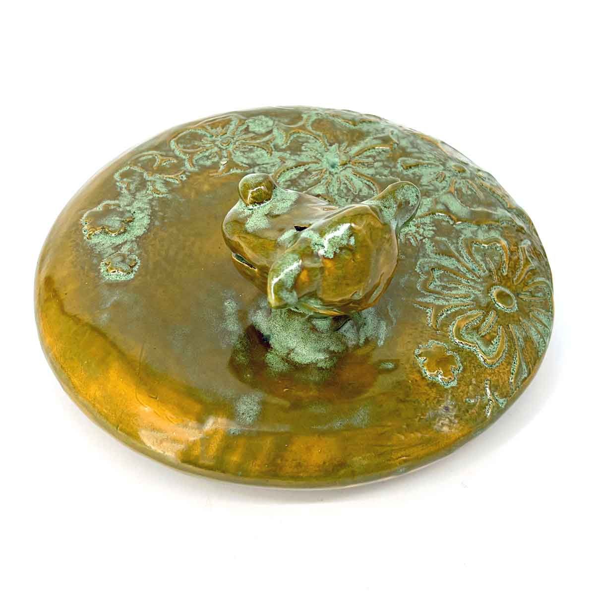 Bronzen kikkerfiguurtje op een rond messing schaaltje, van bovenaf gezien.
