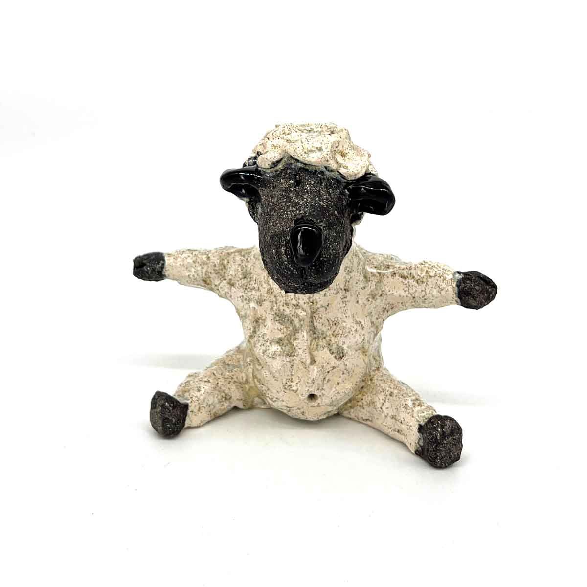 Klein pluche schaapje met beige wol, zwart gezicht en poten, zittend met gespreide benen en armen op een witte achtergrond.