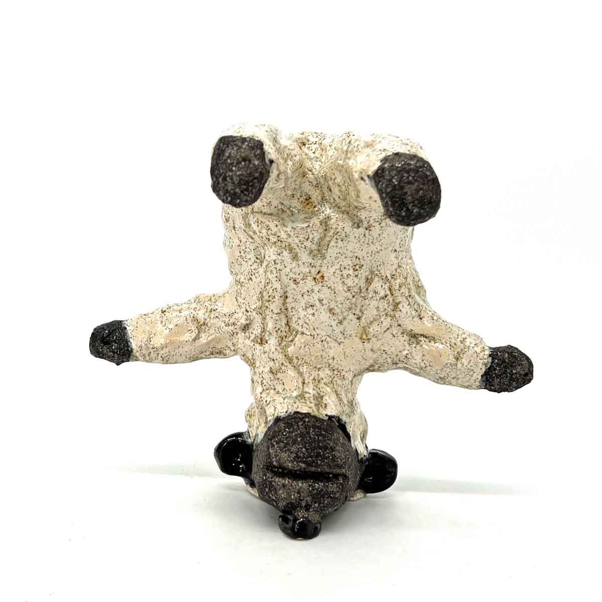 Klein beige knuffeldier met zwarte oren, poten en neus, rechtopstaand op een witte achtergrond.