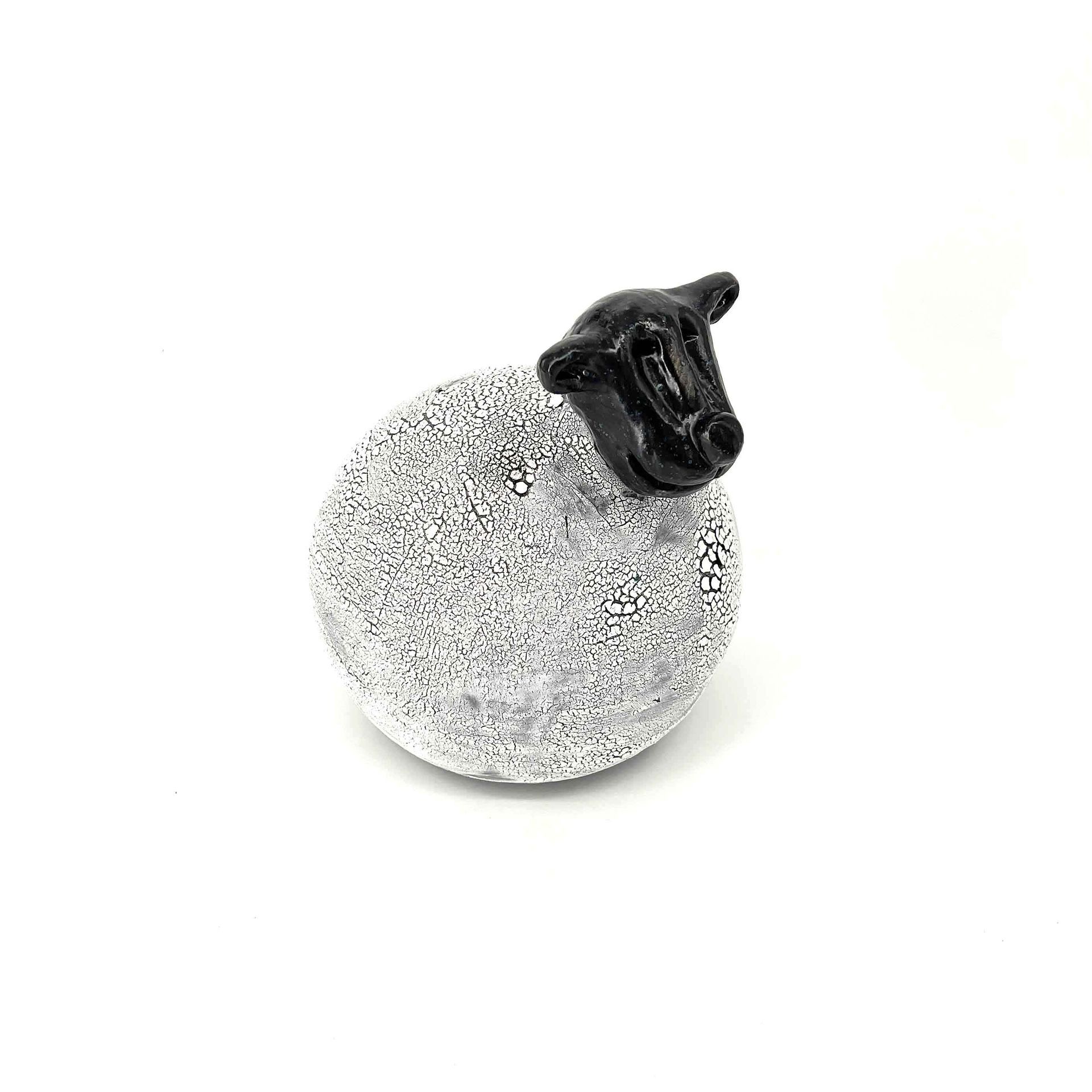 Wit glinsterend ornament met een klein zwart heksenhoedje op een effen witte achtergrond.