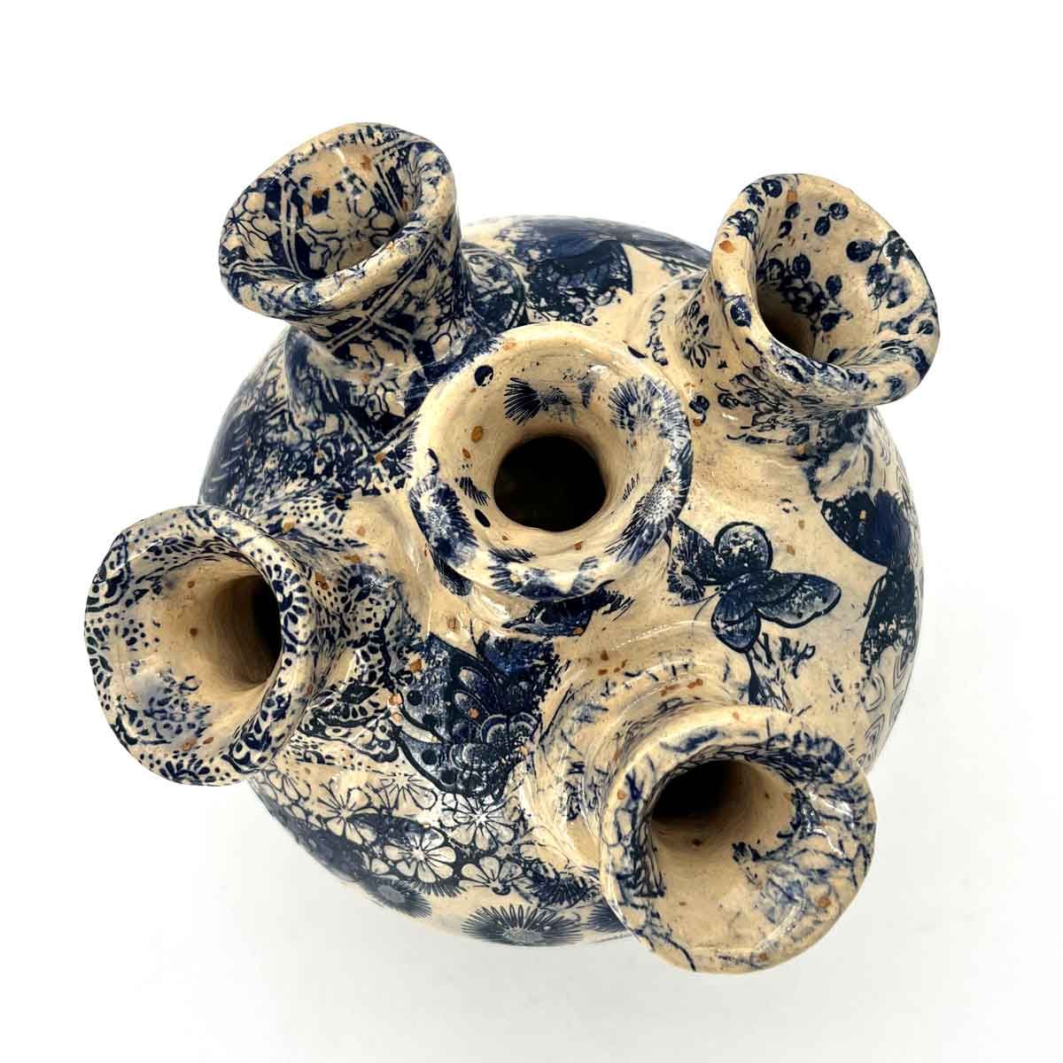 Crème- en blauw gespikkelde keramische vaas met vijf ronde openingen op een witte achtergrond.