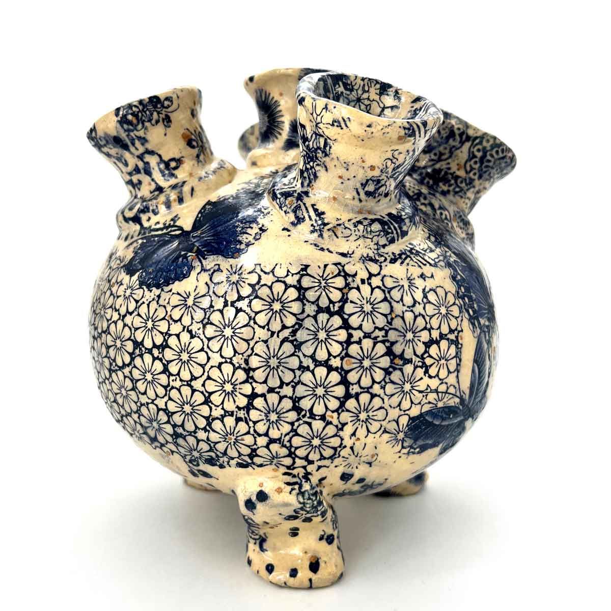 Crème- en blauwkleurige keramische vaas met patroon, een ronde vorm en drie kleine voetjes op een witte achtergrond.