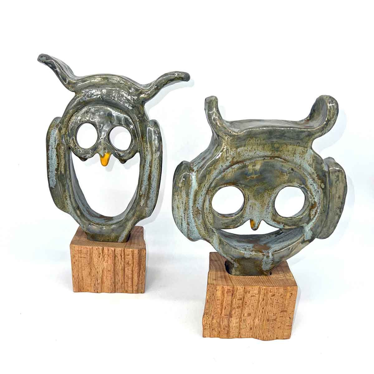 Twee kleine metalen uiltjesbeeldjes met kurken voetjes op een witte achtergrond.