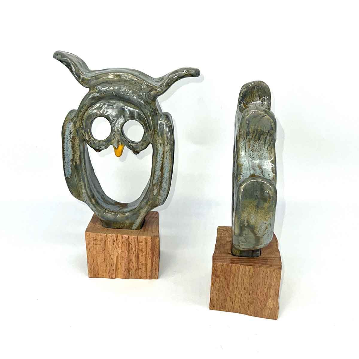 Kleine metalen uilsculptuur, voor- en zijaanzicht, op houten sokkels.