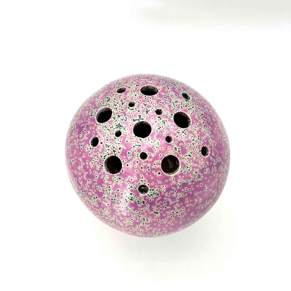 Roze gespikkelde geperforeerde bal met meerdere zwarte gaten op een witte achtergrond