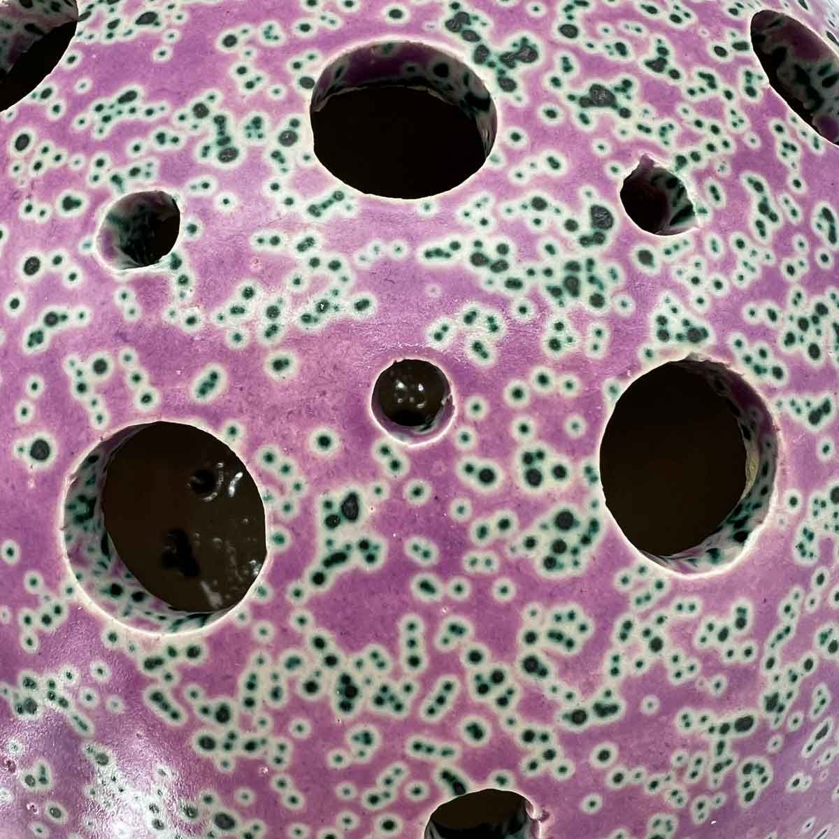 Close-up van een paarse, gevlekte, geperforeerde bol met meerdere ronde gaten.