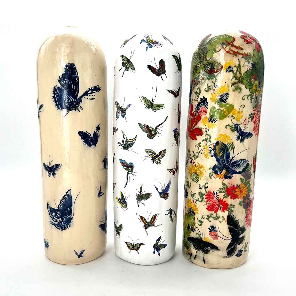 Drie decoratieve keramische vazen ​​met vlinder- en bloemenmotieven in blauw, wit en meerdere kleuren.