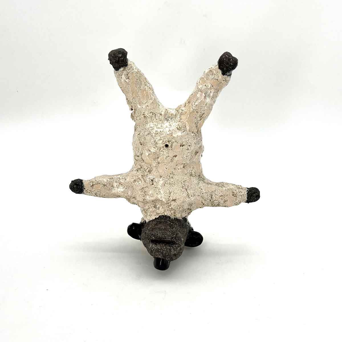 Klein beige beeldje met zwarte uiteinden, ondersteboven op een witte achtergrond.