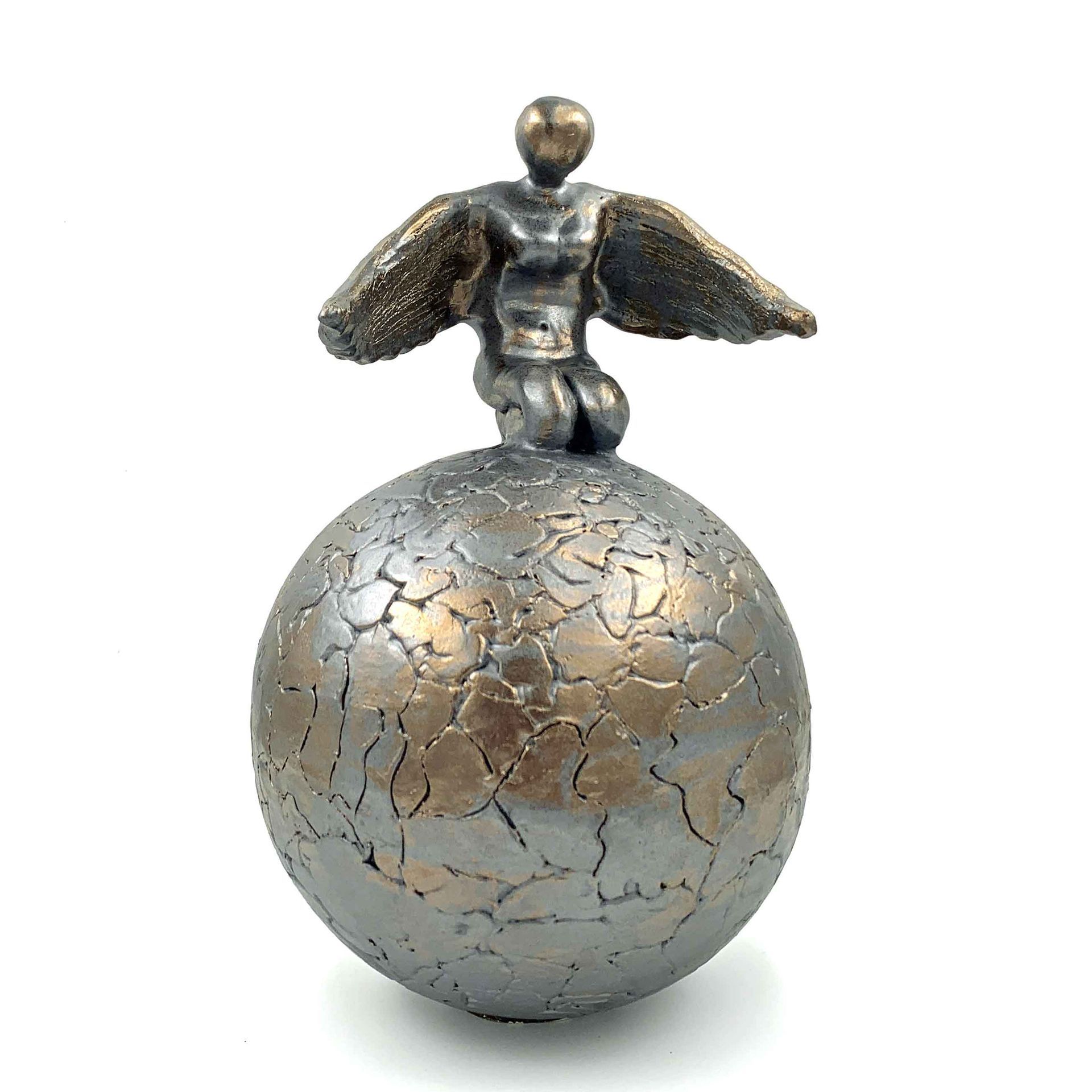 Klein bronzen beeldje met vleugels, zittend op een gebarsten metalen bol, geïsoleerd op een witte achtergrond.