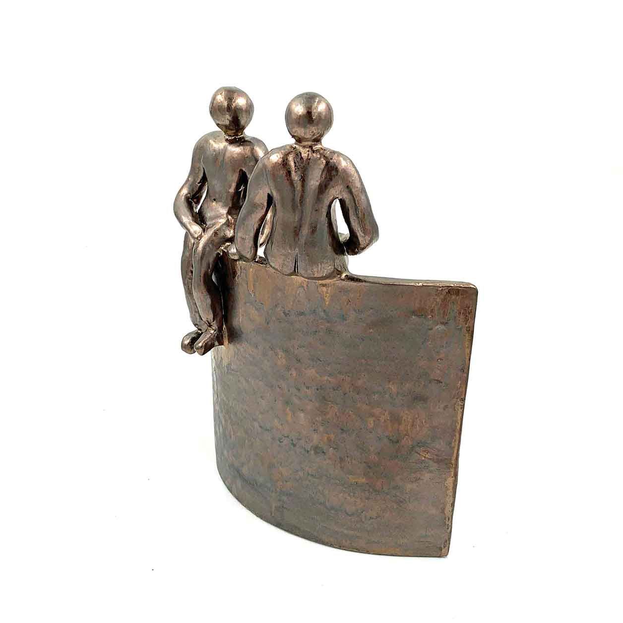 Twee kleine metalen figuurtjes zitten op een gebogen bronzen sokkel.