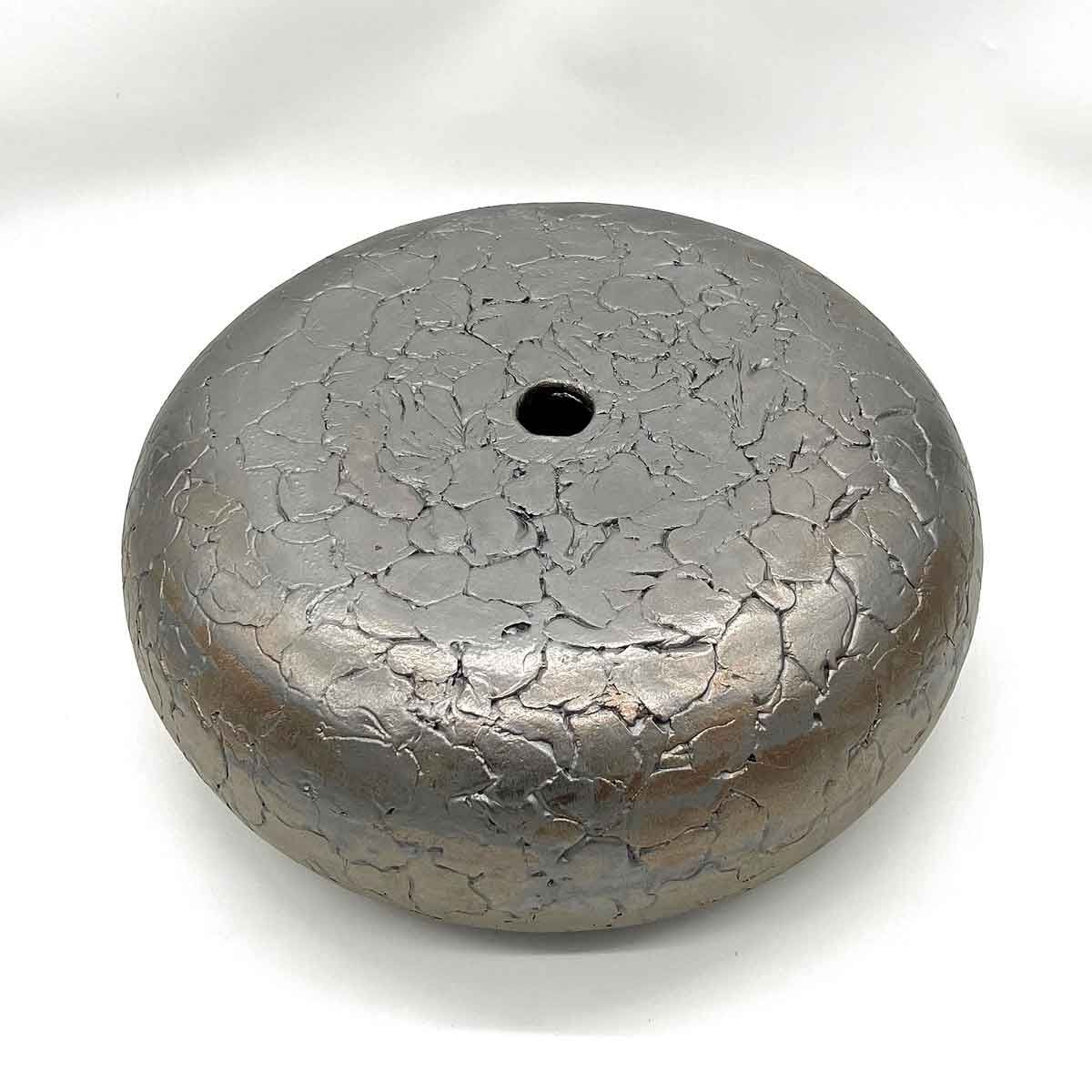 Rond, zilverkleurig, gebarsten metalen gewicht met een klein gaatje in het midden.