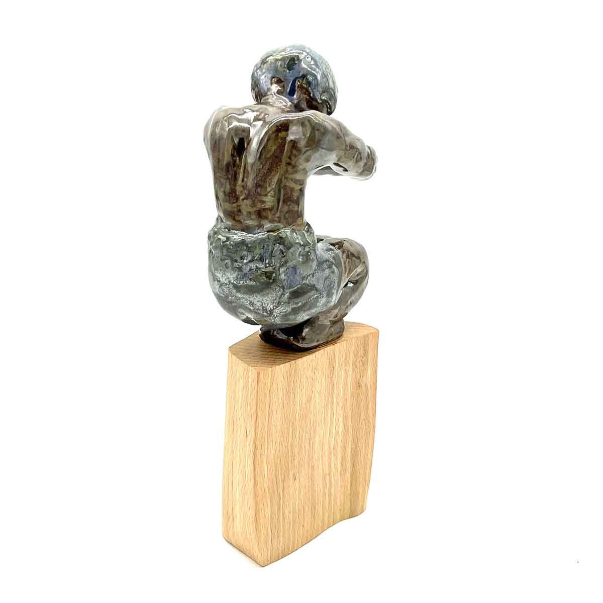 Klein abstract bronzen beeldje, gehurkt op een rechthoekige houten sokkel.