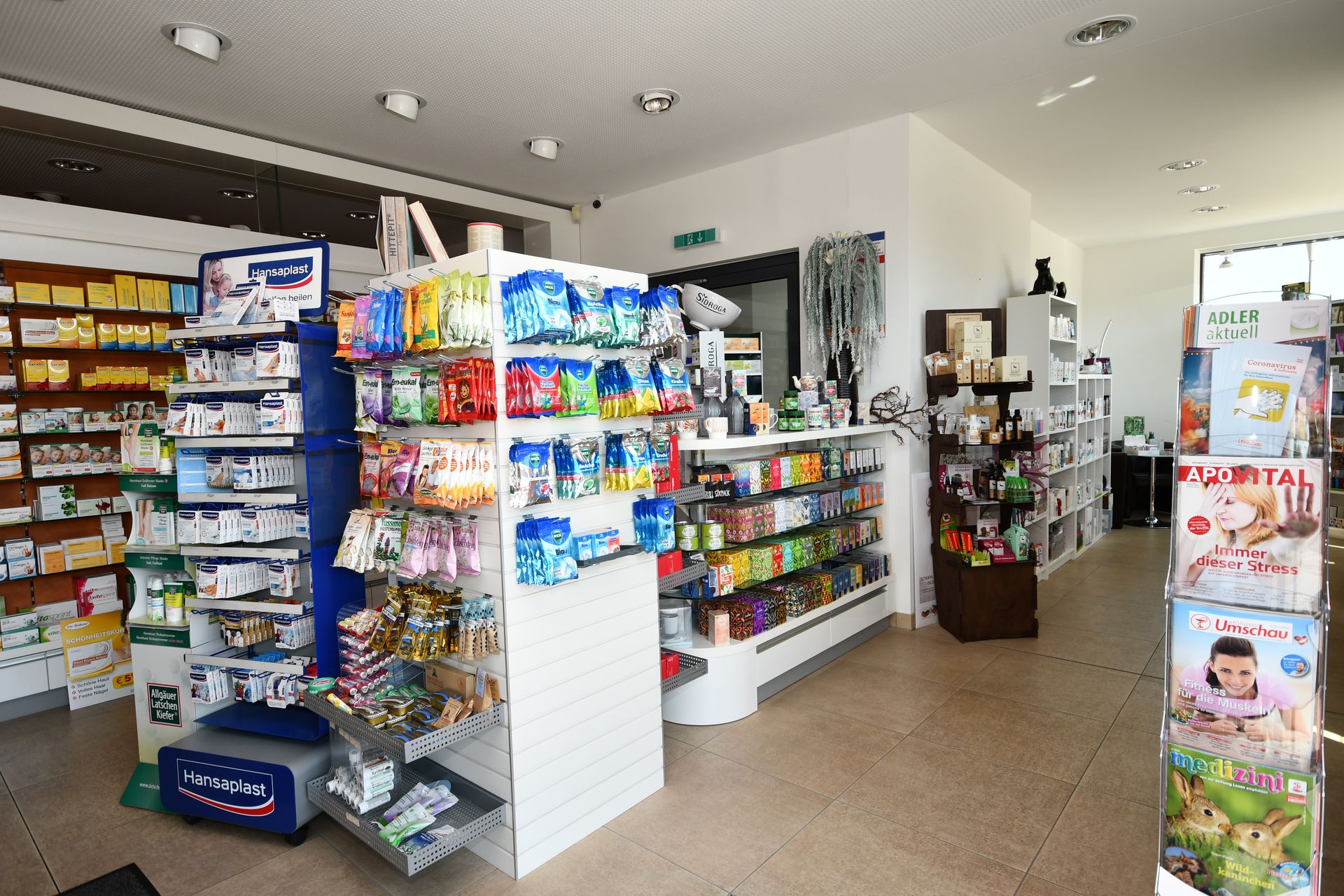 Innenansicht einer Apotheke mit Regalen voller Produkte und einem zentralen Auslagebereich. 