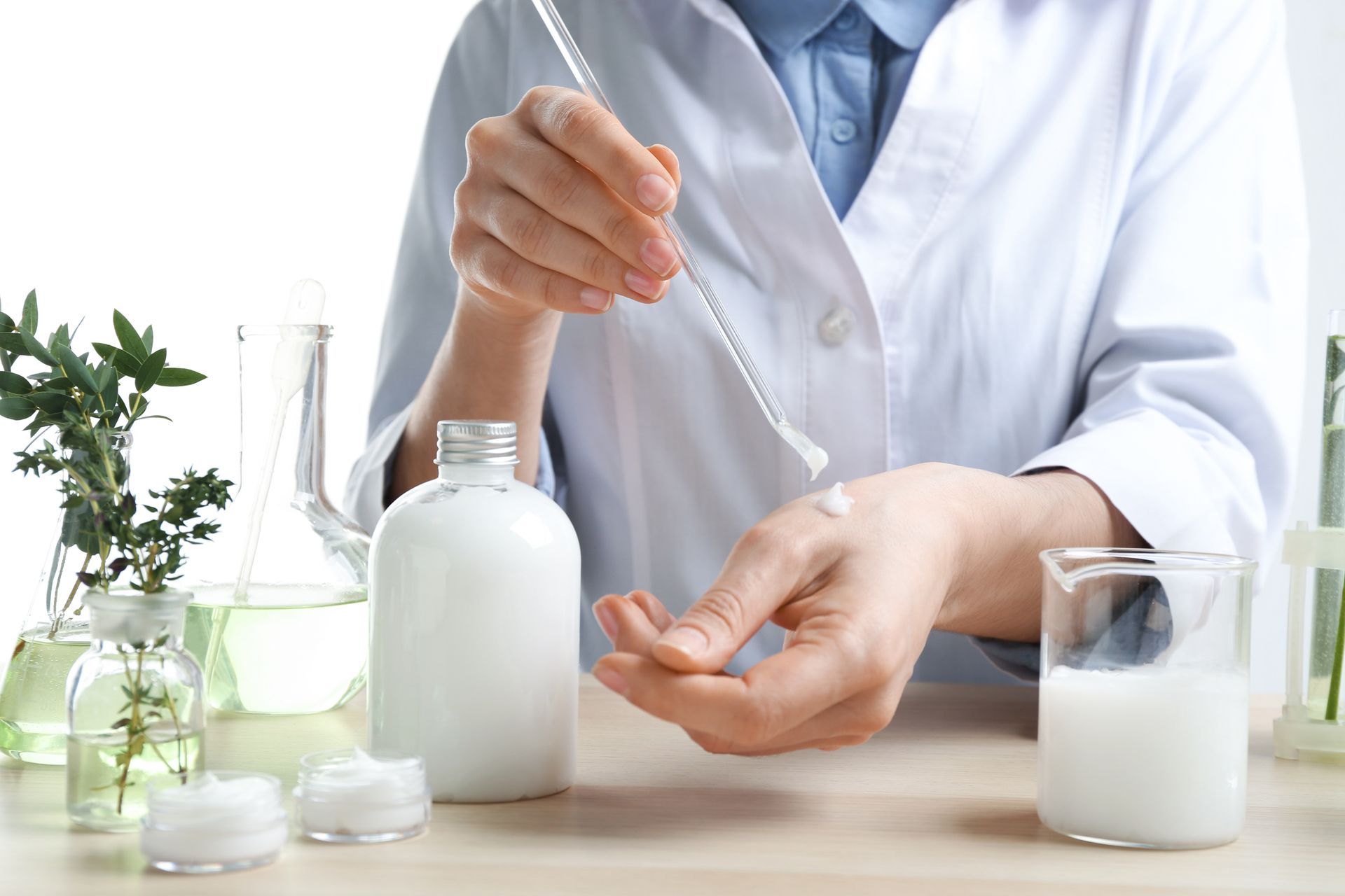 Wissenschaftler im Laborkittel testet Kosmetikcreme auf der Hand, Laborgeräte im Hintergrund.