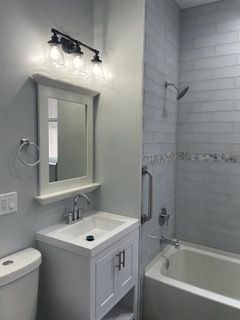 Small bathroom with white vanity, mirror, sink, and bathtub with tiled shower walls.