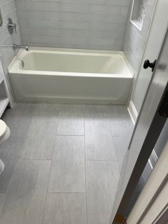 Small bathroom with a white bathtub, gray tile floor, and tiled walls.
