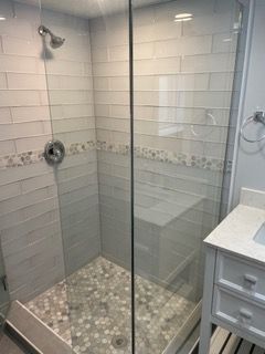 Tiled walk-in shower with glass door, pebble floor, and built-in niche in a bathroom