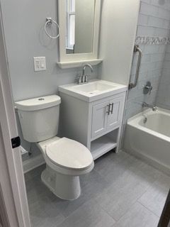 Small bathroom with toilet, sink vanity, mirror, and tub shower on gray tile floor.