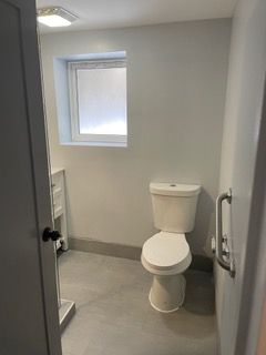 Small gray bathroom with a toilet, window, and partially open door.