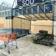 Garden center entrance with stacked sod rolls, shopping cart, and black awning over a concrete walkway