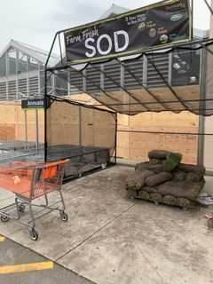 Outdoor garden center cart corral under a metal canopy, with stacked sod and an orange shopping cart.