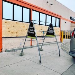 Two black A-frame signs with boarded storefront windows behind them outside a store entrance