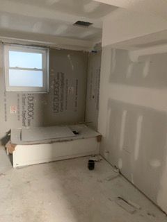 Unfinished bedroom with drywall patches, a window, and a bed frame on the floor
