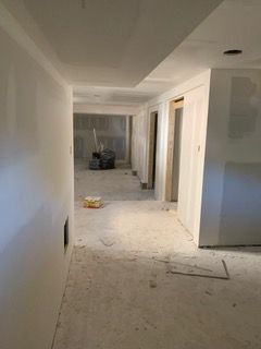 Unfinished hallway interior with drywall, dust-covered floor, and construction materials.