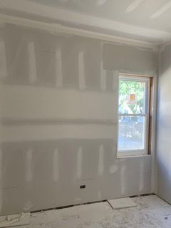 Unfinished drywall room with a window and white patching on the walls and floor coverings.