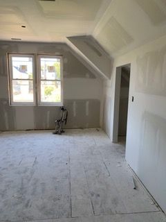 Unfinished room with drywall, sloped ceiling, two windows, and a doorway under construction.