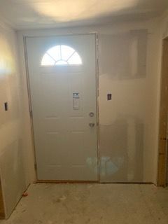 Front entryway with white door, small arched window, and bare walls under renovation
