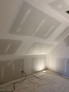 Empty room under construction with drywall patches, bare floor, and a work light near the wall
