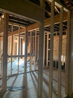 Unfinished room with exposed wooden framing, beams, and sunlight streaming through open windows.