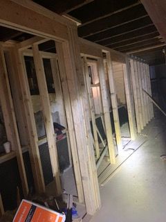 Wood-framed hallway under construction, with exposed studs and a flashlight illuminating the floor.