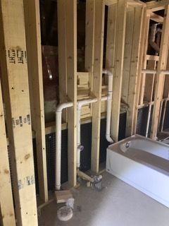 Unfinished bathroom framing with exposed studs, plumbing pipes, and a bathtub under installation.